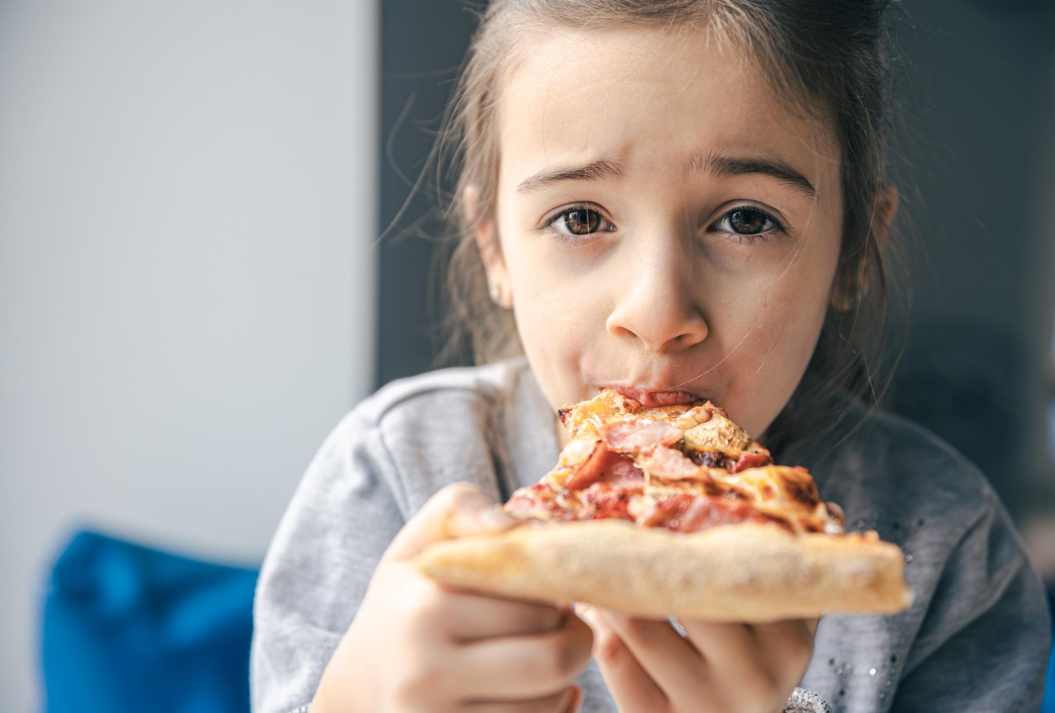 Small girl is eating pizza and looking at camera.