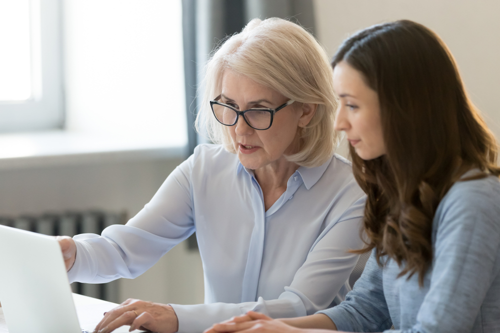 Older female employee asking younger colleague for help with her tasks