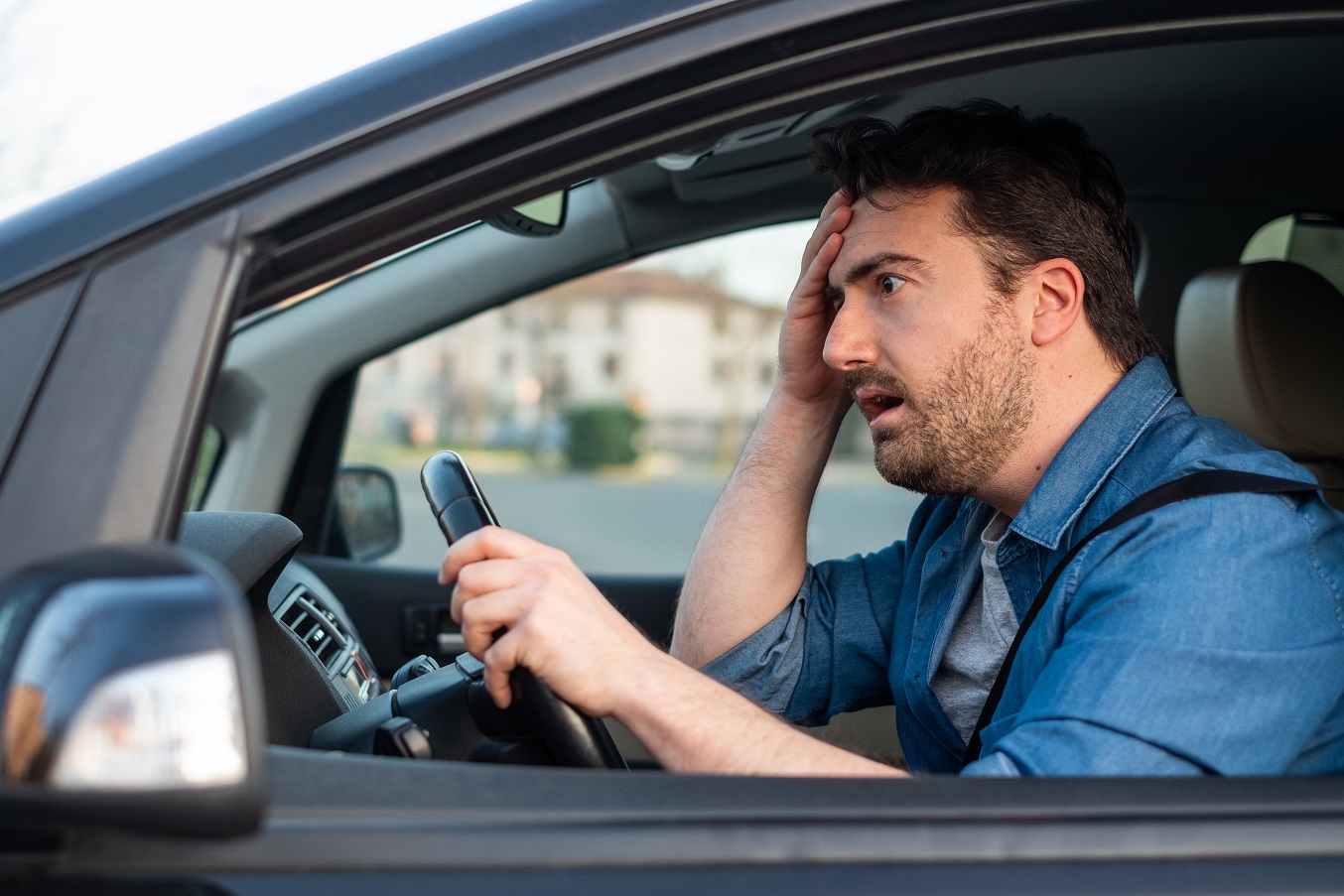 Bearded man with blue shirt is driving a car with a shocked face.