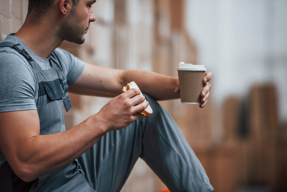 Employee sitting and having a break, eating sandwich and drinking coffee.