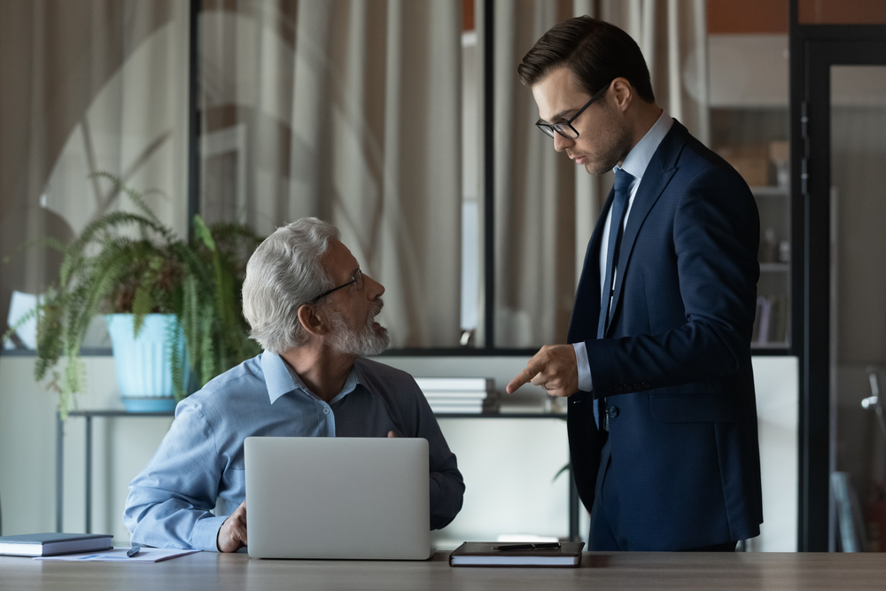 Angry employee at his boss pointing finger accusing him of something standing over his desk