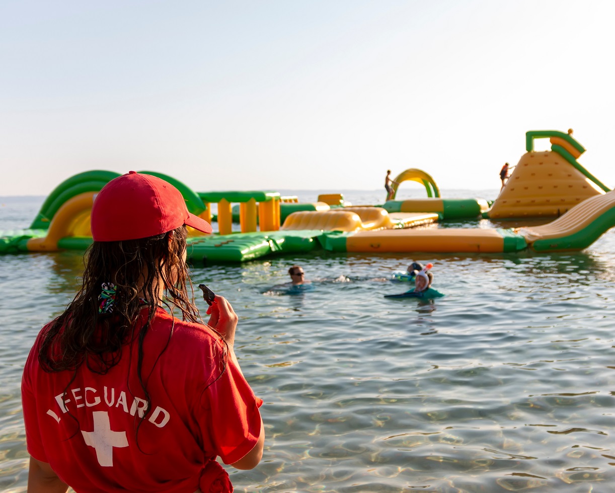 Female lifeguard on rescue duty, standing on shore with whistle.