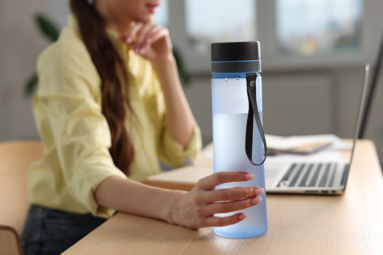 Woman holding transparent bottle at workplace indoors, closeup