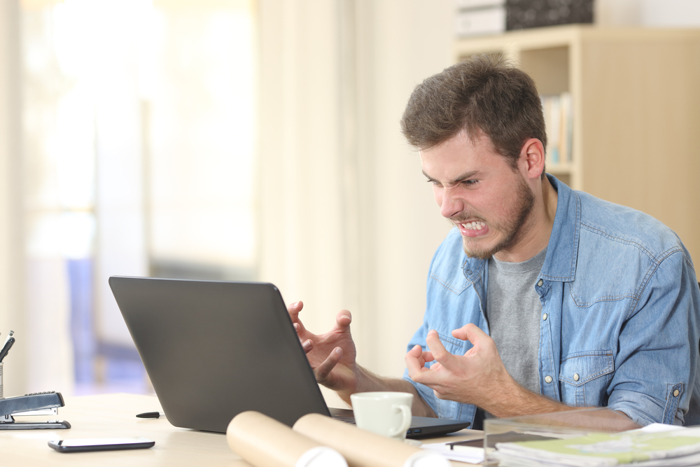 Angry man sitting at his desk in front of a computer looking at the computer