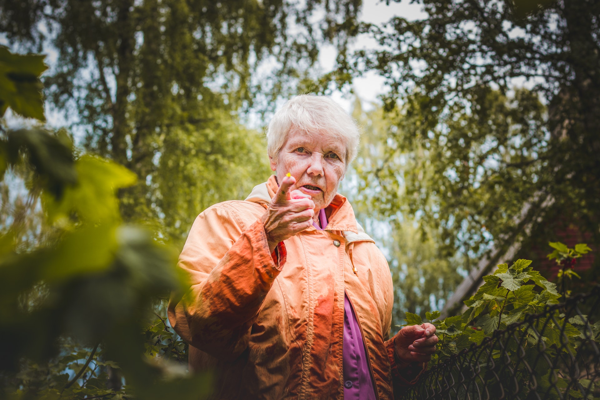Older woman pointing at the camera near a fence