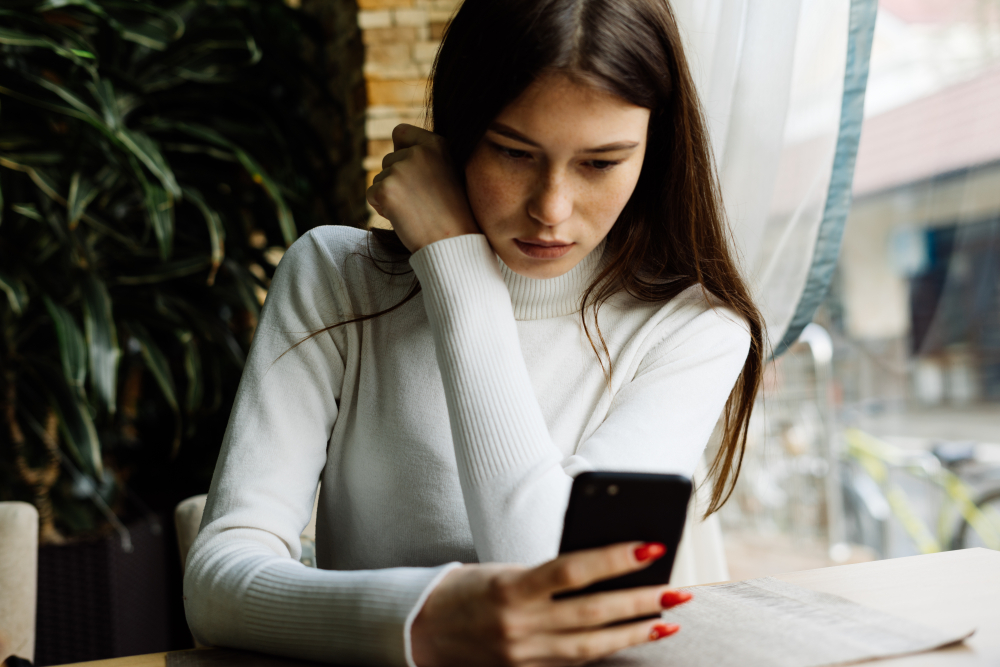 Young girl  sits in a café and looks at a smartphone
