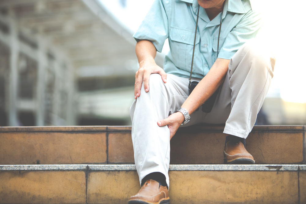 Unhappy senior man suffering from knee ache sitting on stairs holding his knee
