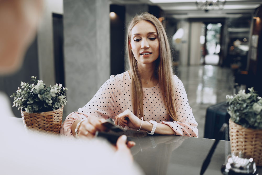 Young beautiful woman hotel guest paying for her stay with credit card at front desk