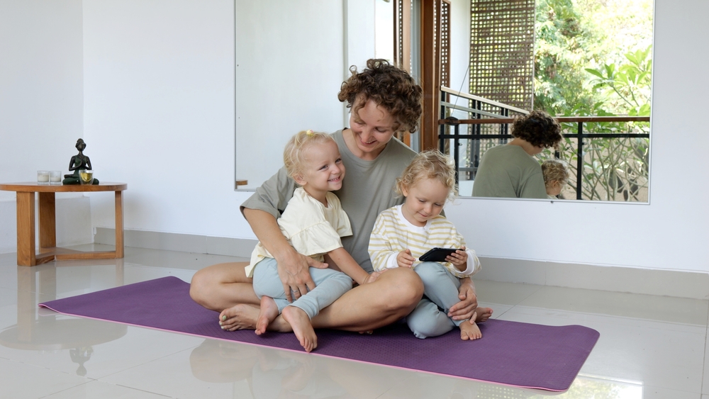 A young mother of twin girls sits with them on the floor