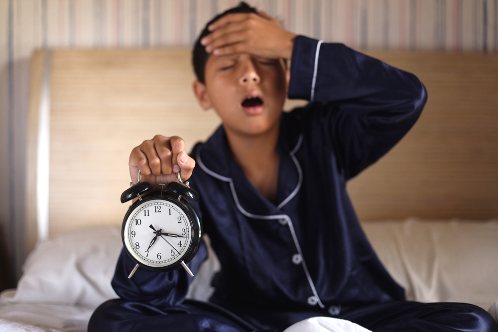 Shocked boy got up of bed and holds his forehead with his arm feeling pain
