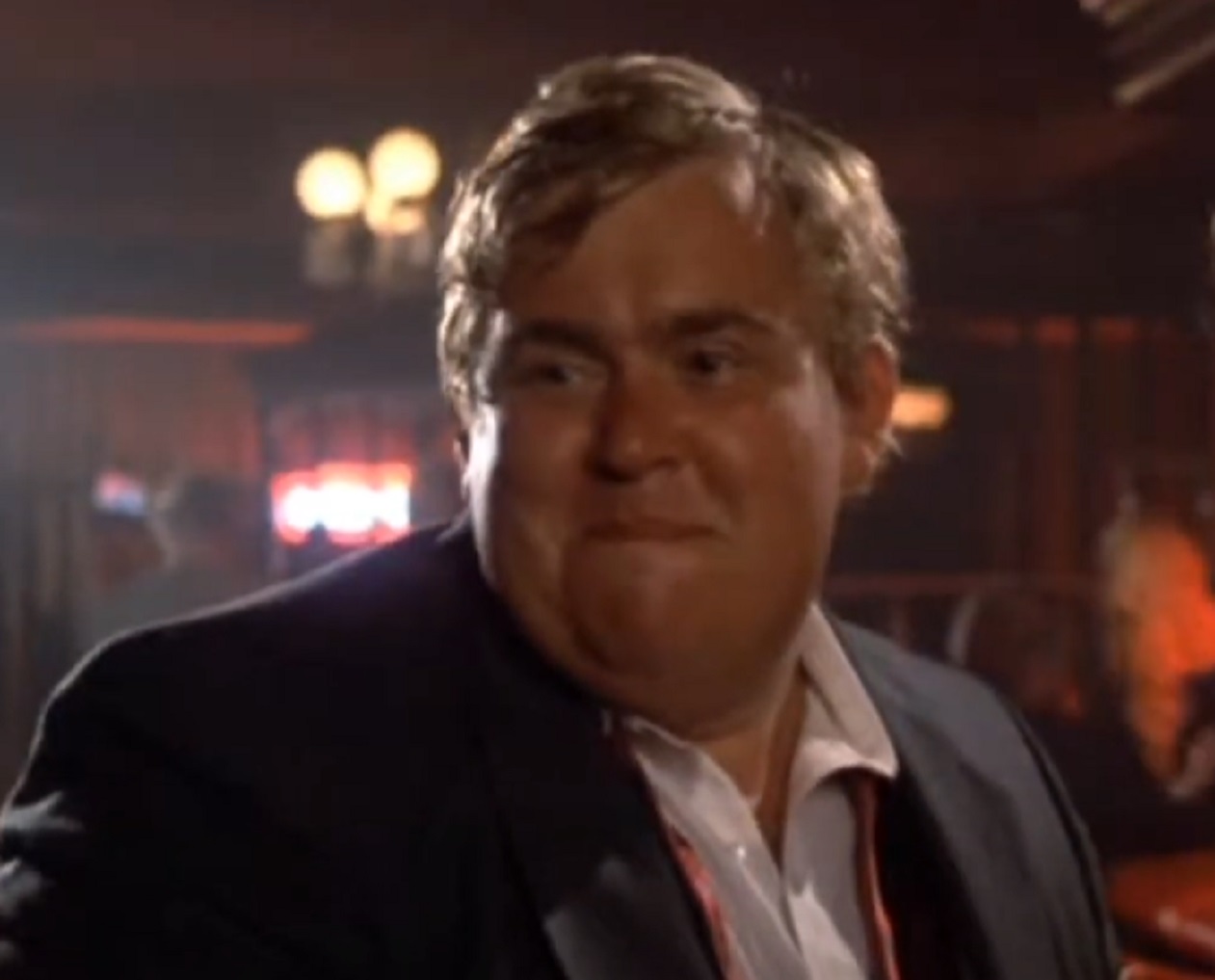 Screenshot :John Candy wearing black suit and white shirt is looking at side with upset face - from Splash (1984)