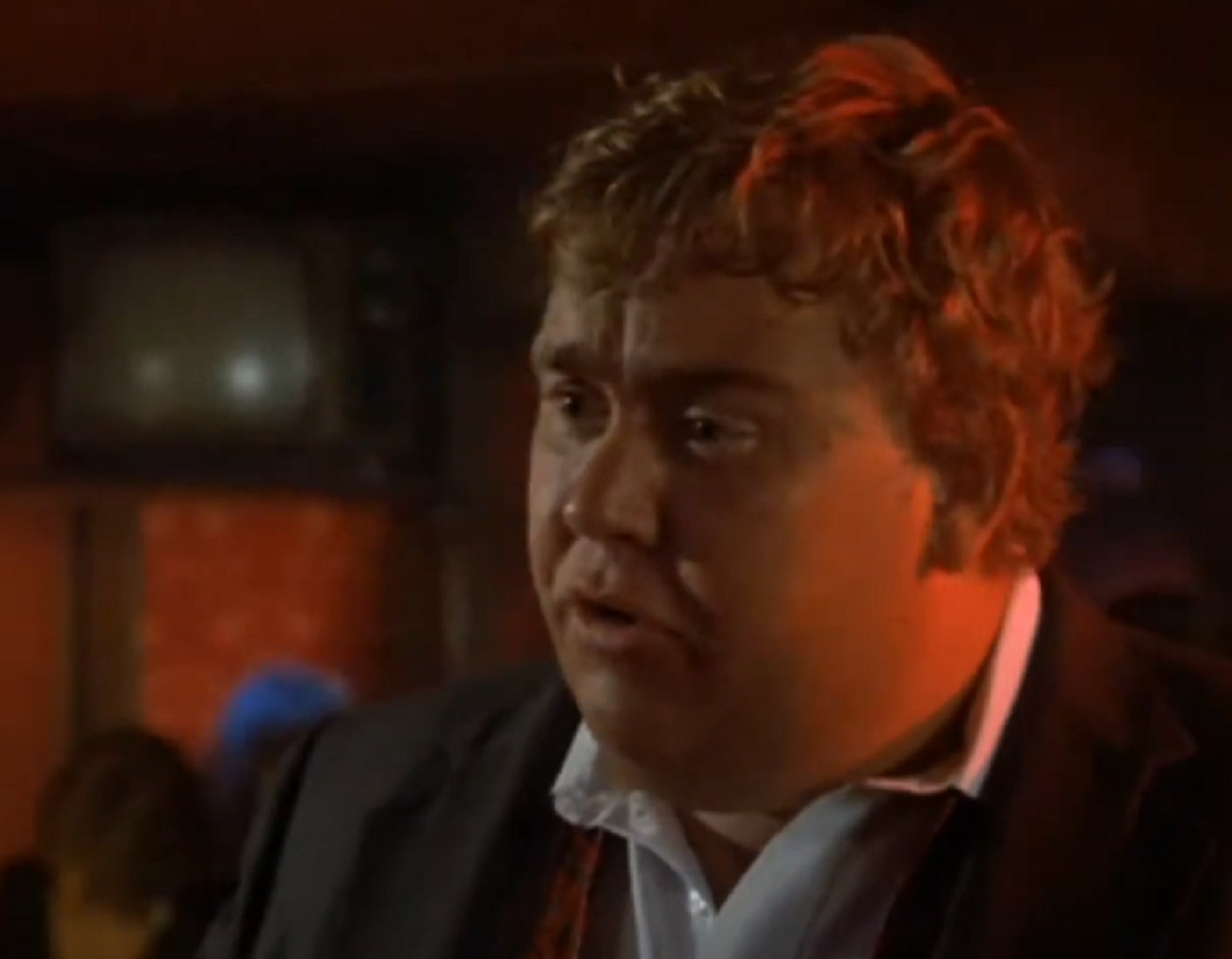 Screenshot :John Candy wearing black suit and white shirt is looking at side - from Splash (1984).