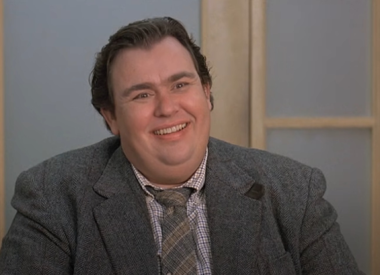 Screenshot :John Candy wearing grey suit is smiling at camera - from Uncle Buck (1989)