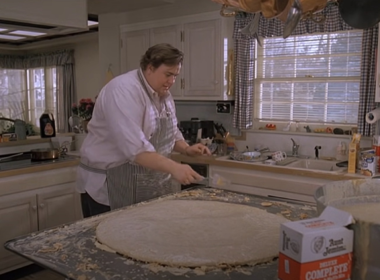 Screenshot :John Candy wearing white shirt is making a pizza in the kitchen - from Uncle Buck (1989)