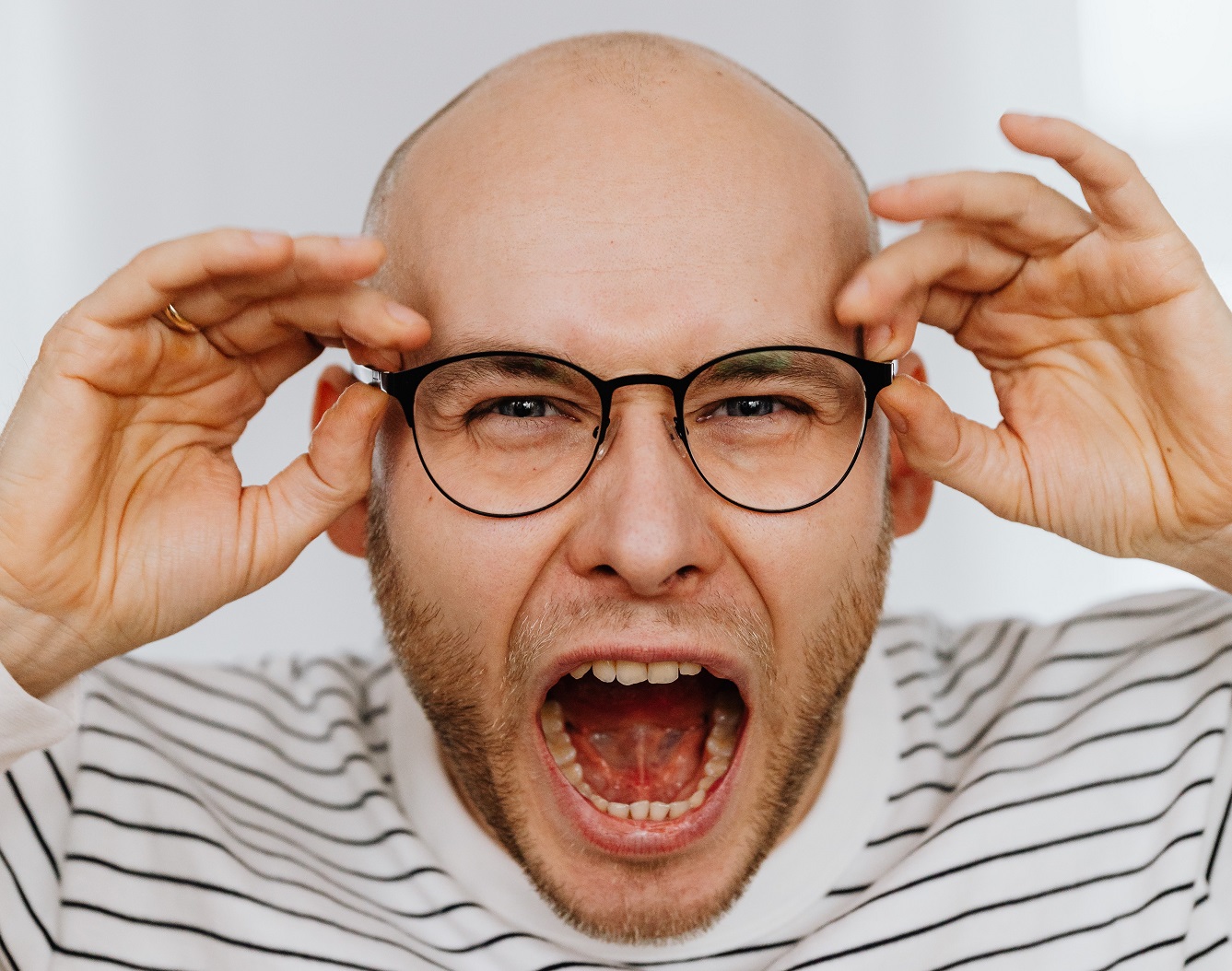 Young bold man wearing glasses is screaming at camera.