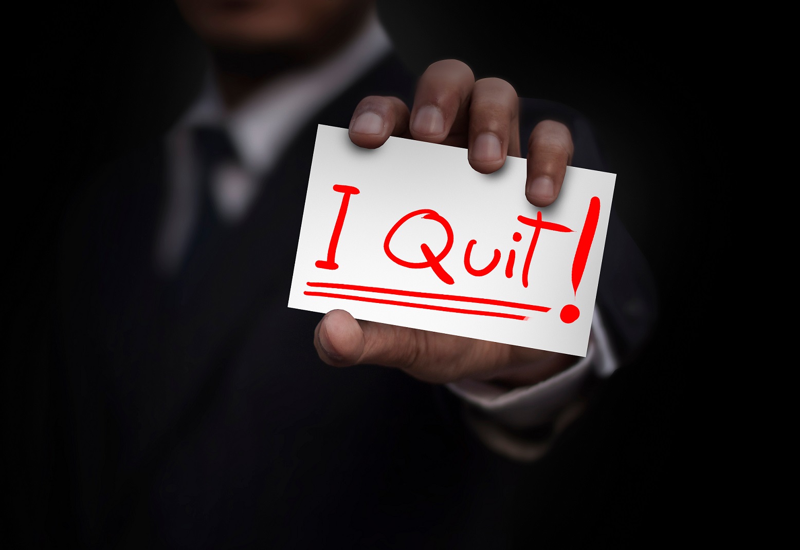Businessman wearing dark suit is showing word I quit on paper.
