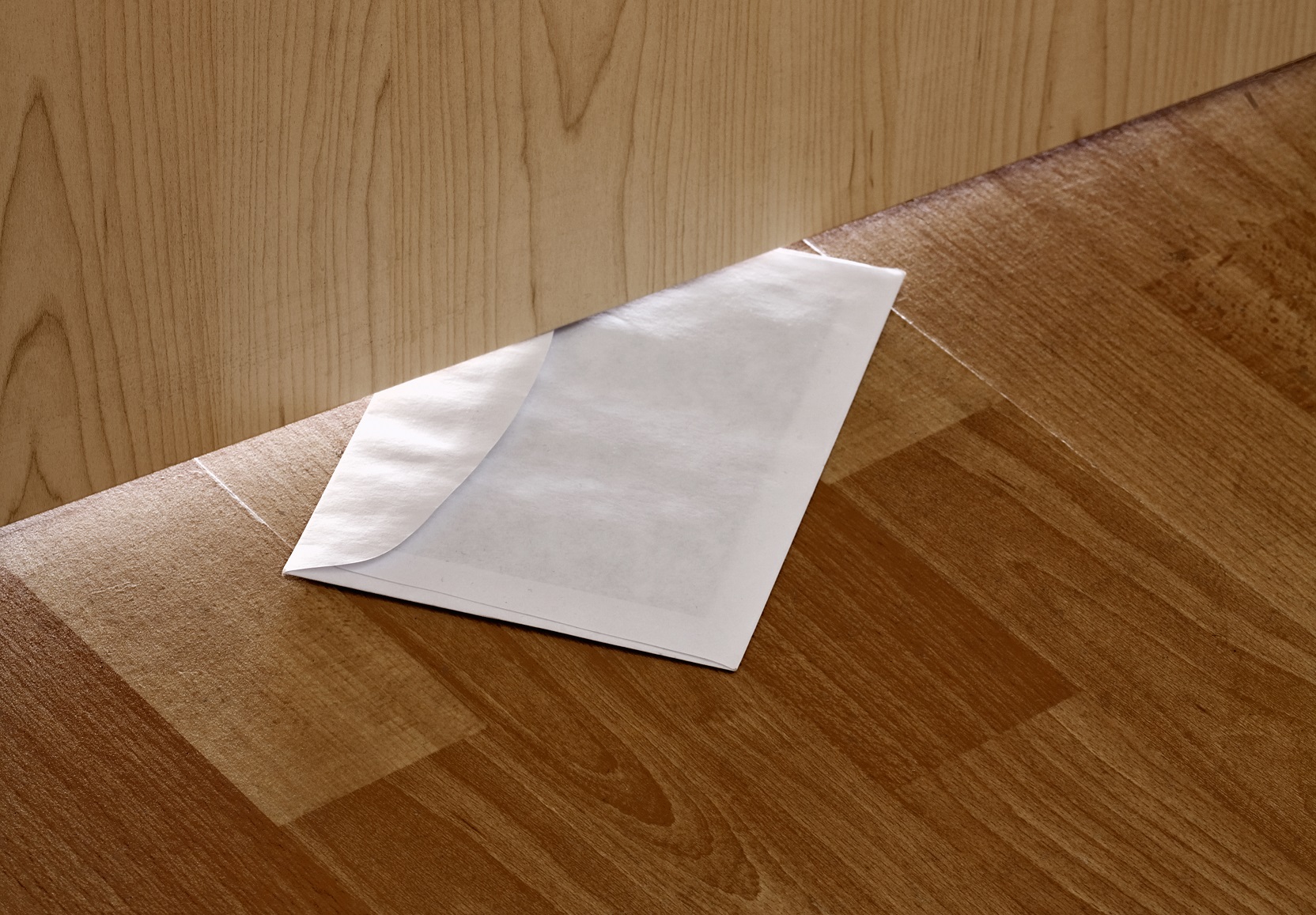 White envelope with message slipped under wooden door.