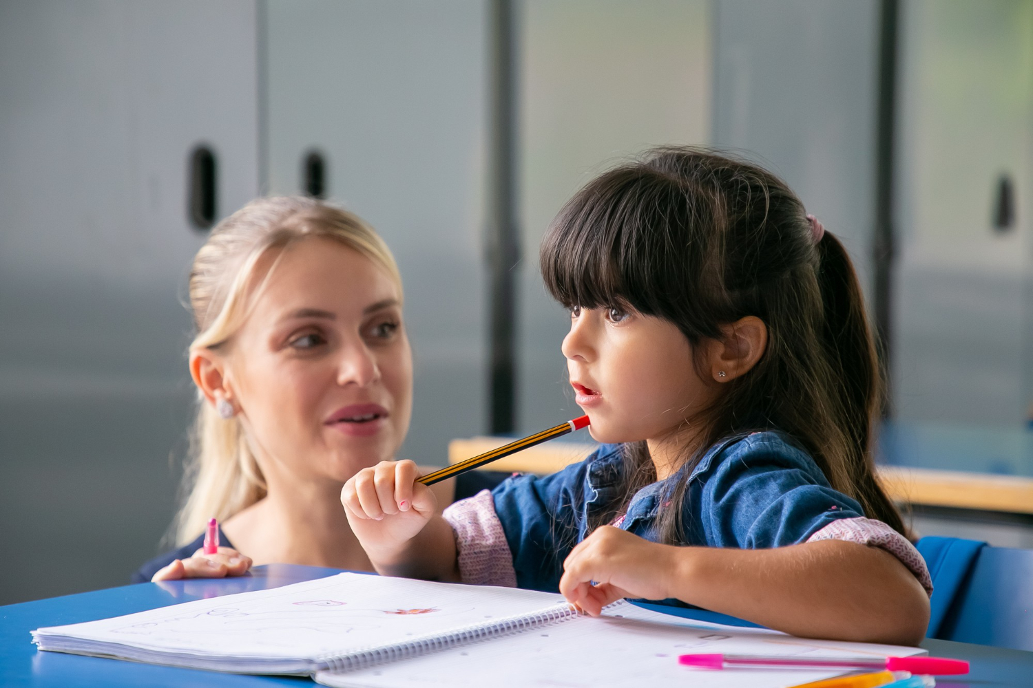 Small girl wearing blue shirt is talking with a teacher at class.