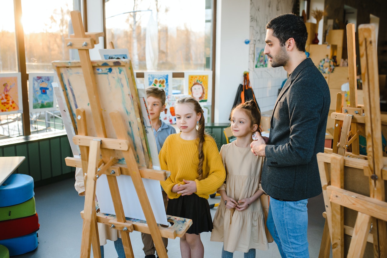 Teacher wearing black coat is teaching small kids in art class.