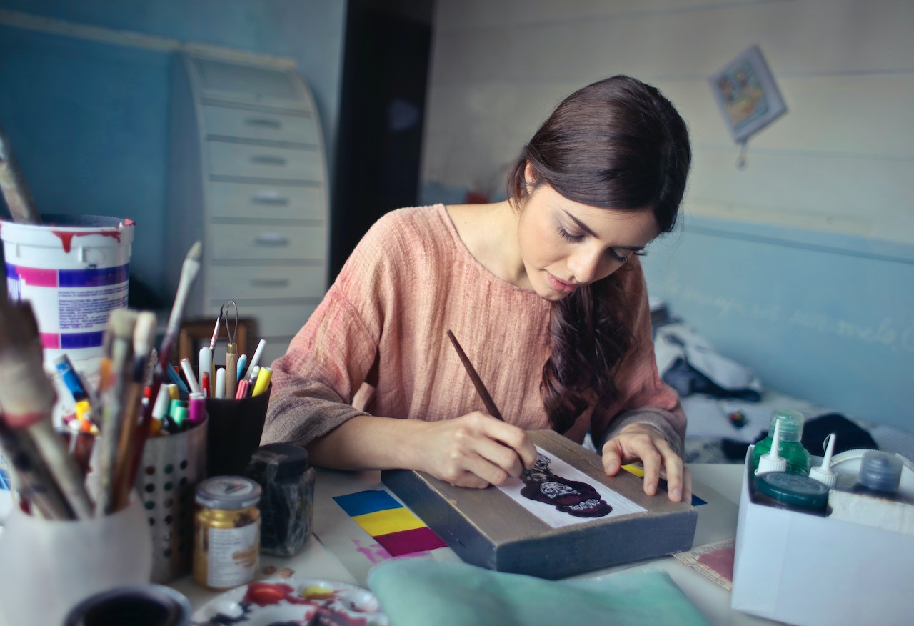 Young girl with long hair and pink shirt is painting a image.
