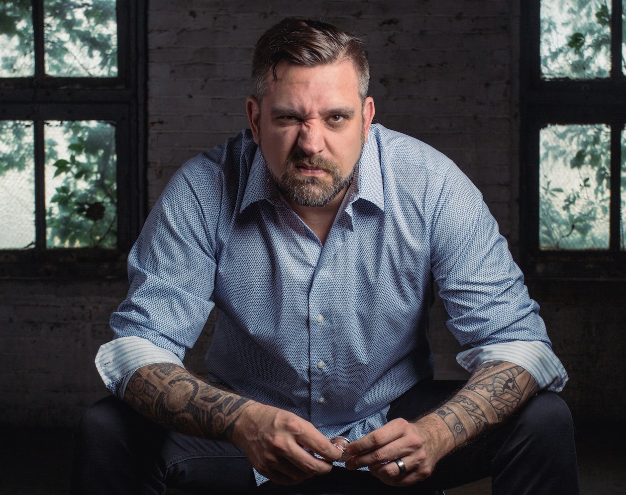 Man with tattoo is looking at camera with angry face.