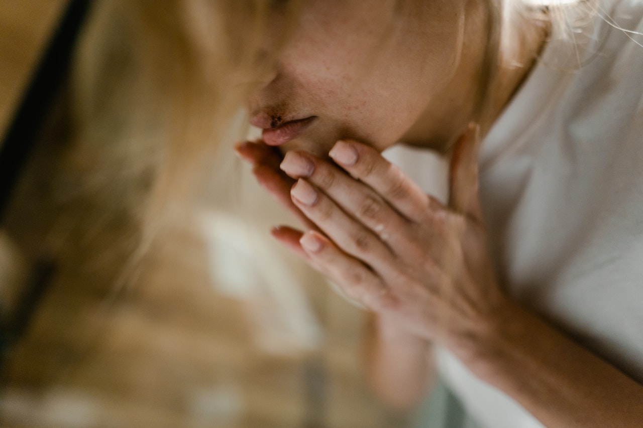 A female person with bruised lips is looking at mirror.