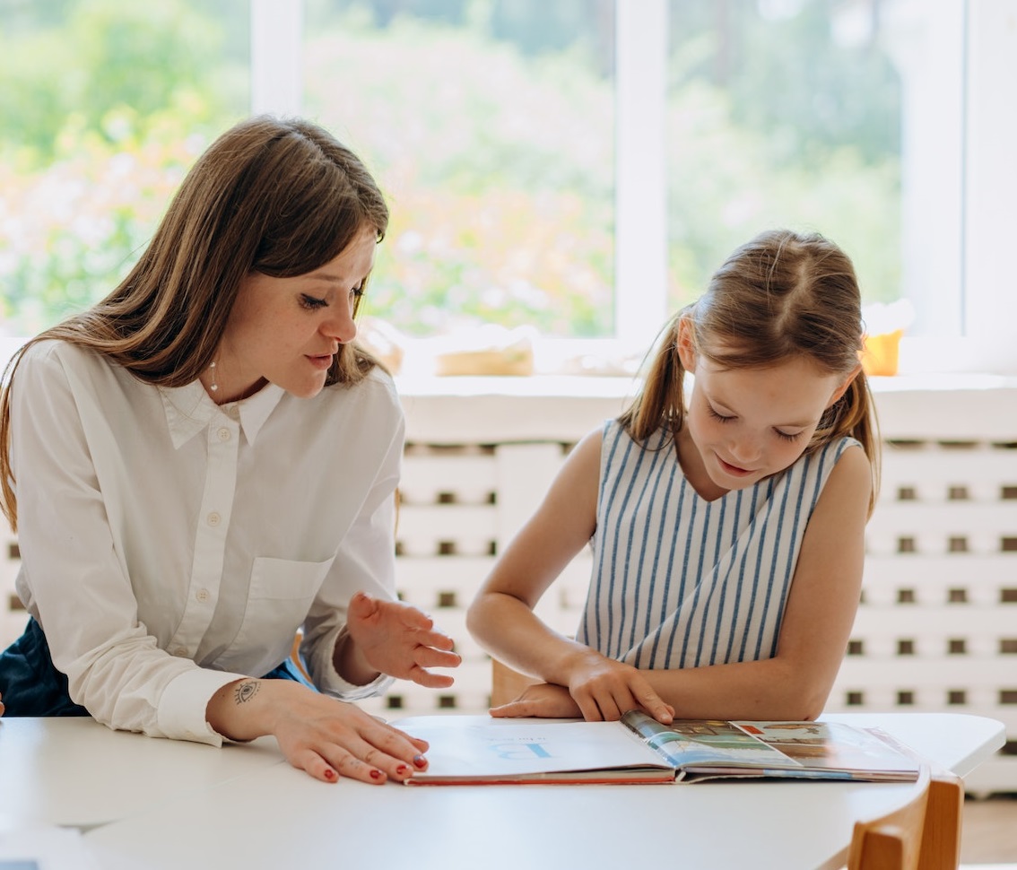 Young female teacher is studying with small girl in classroom.
