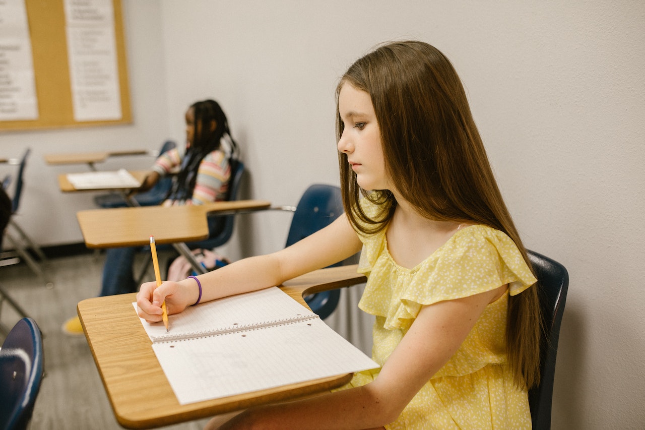 Young girl is seating on bench at classroom.
