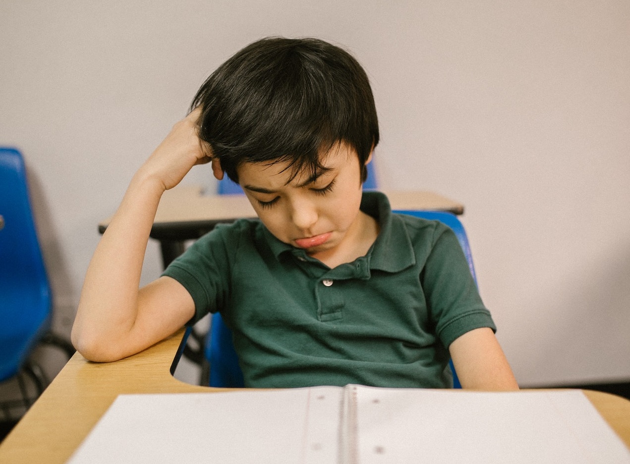 Sad kid is seating alone in classroom an crying.