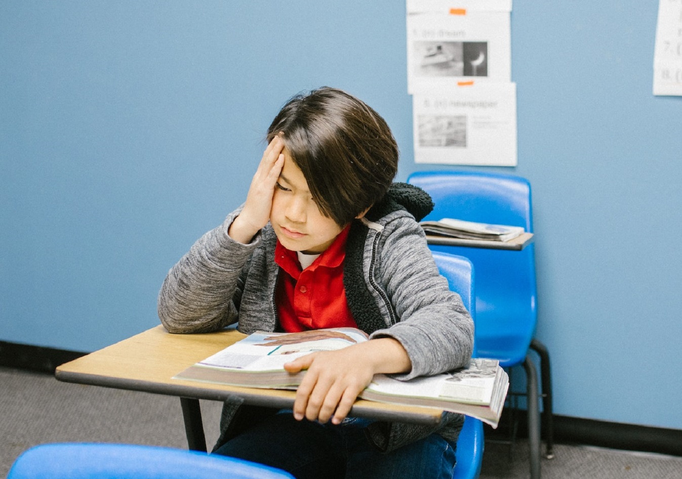 Sad young kid seating in school bench is looking down.