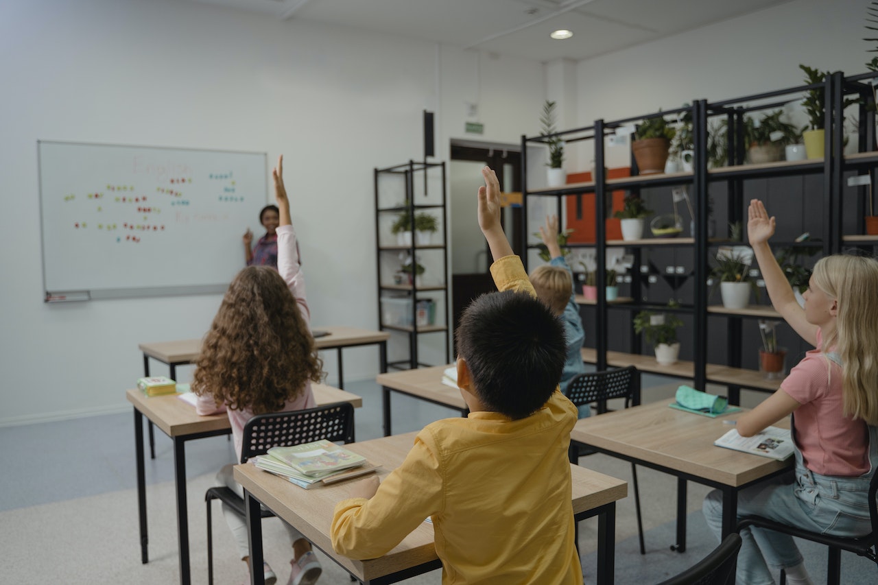 Students with their hands raised is looking at teacher.