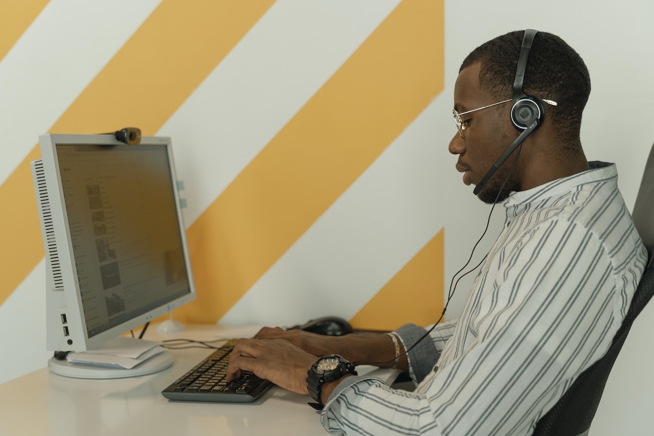 Young man wearing headset is working on a pc and making calls.