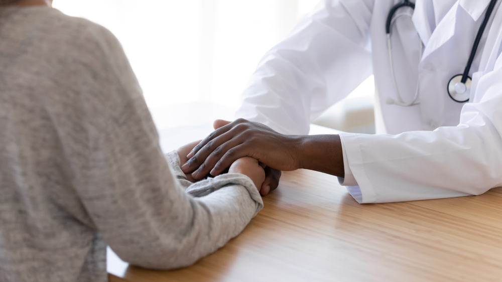 Black male doctor holding hands of female patient