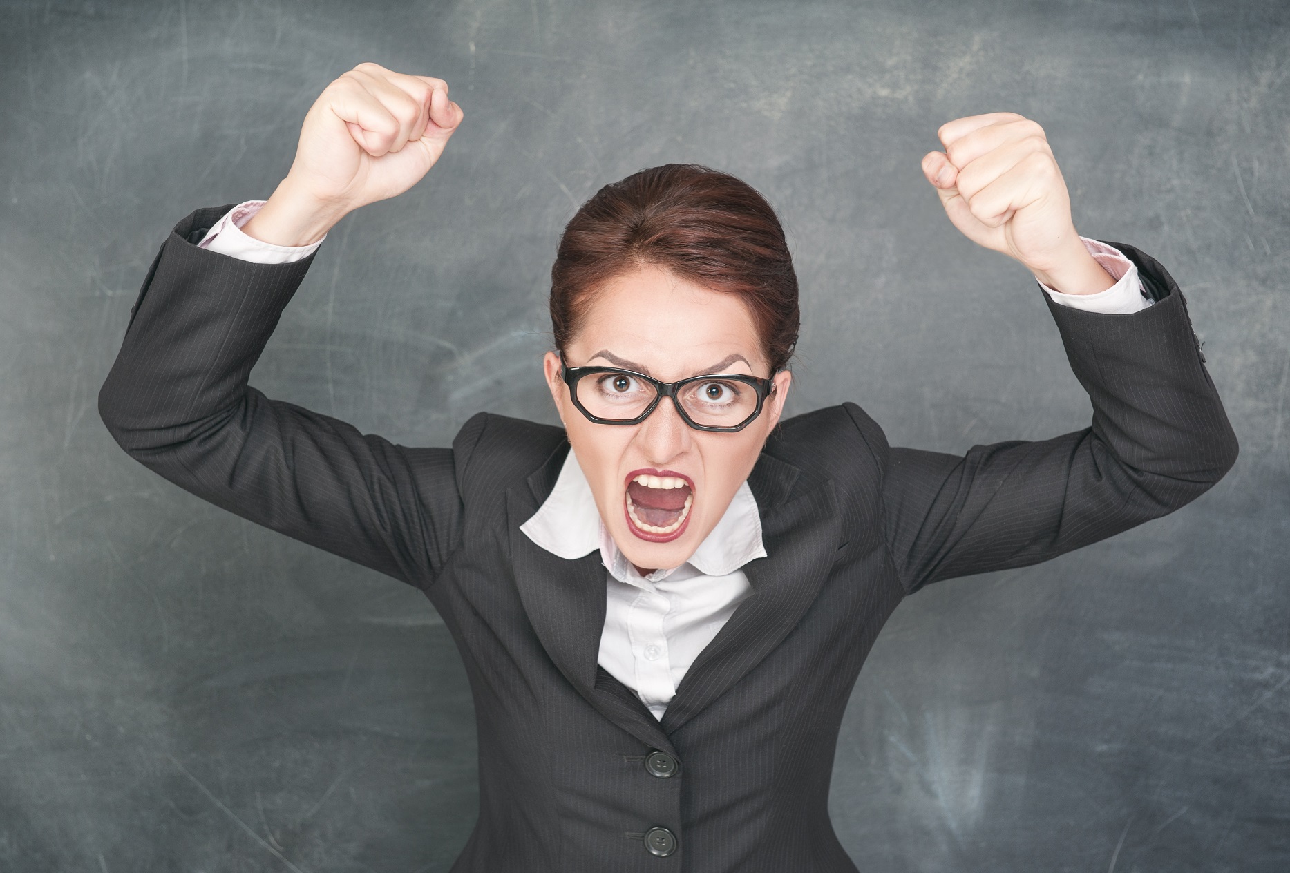 Angry woman wearing black suit is standing in front of a blackboard.
