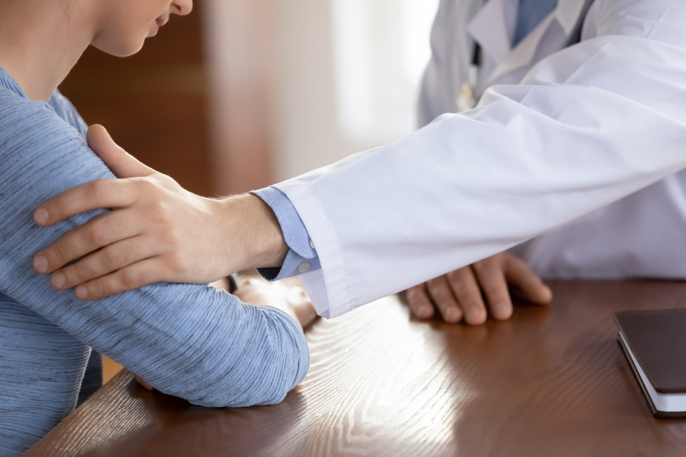 Close up of a caring doctor therapist touching upset frustrated female patient hand at medical appointment