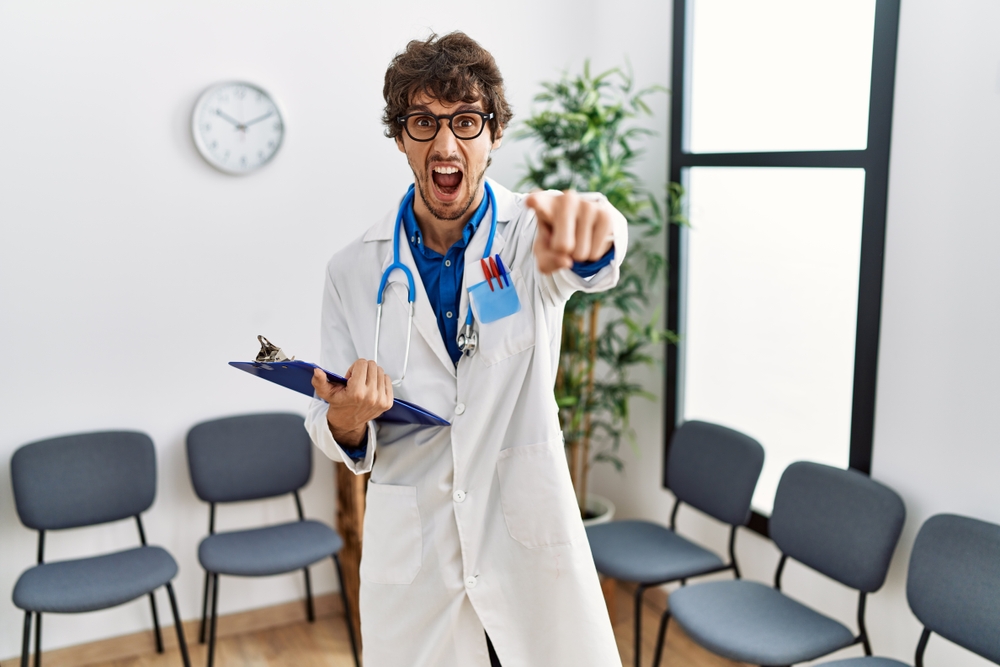 Young Hispanic doctor man at waiting room pointing displeased