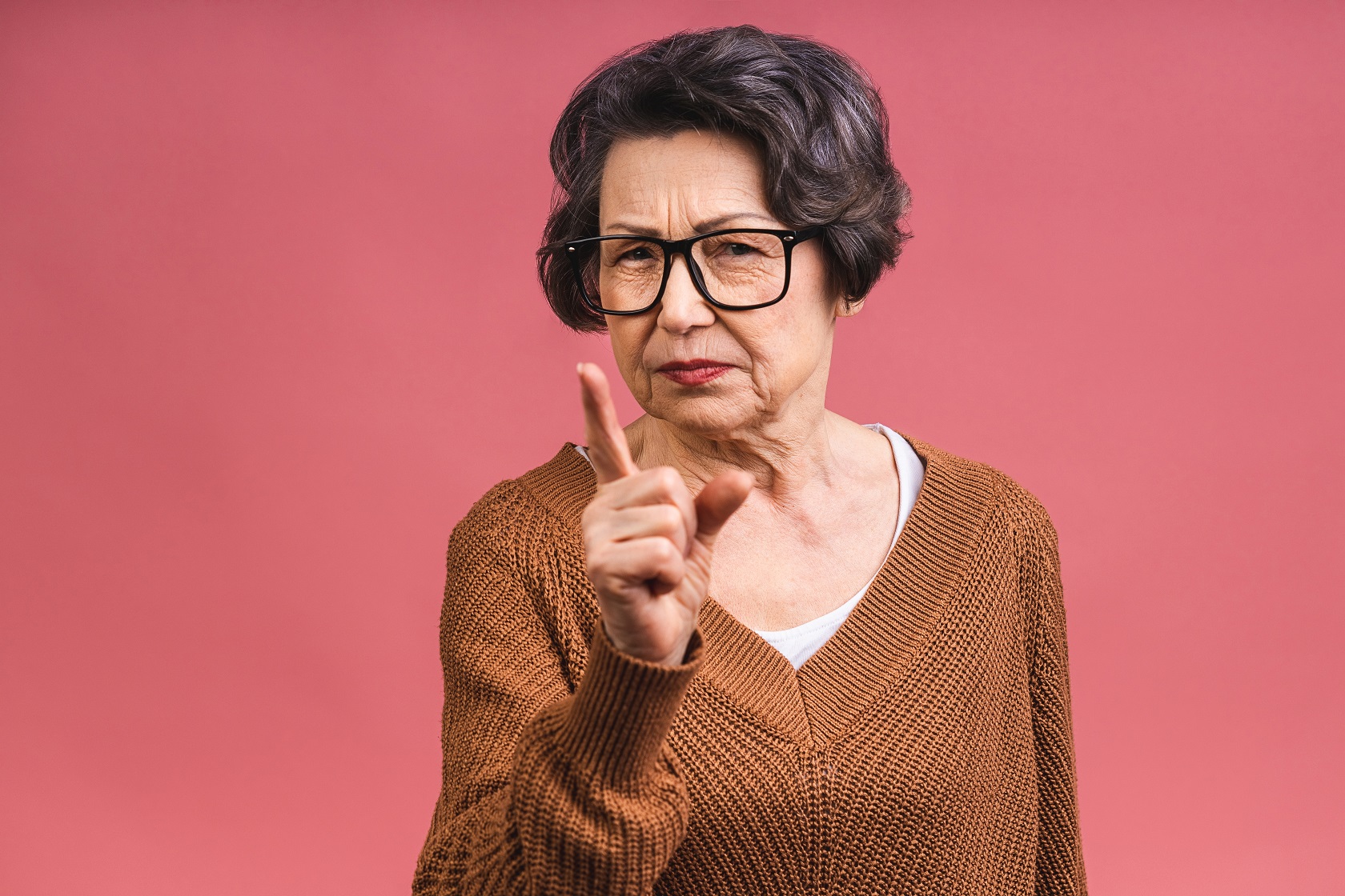 Senior woman is pointing with finger to a camera on red background.