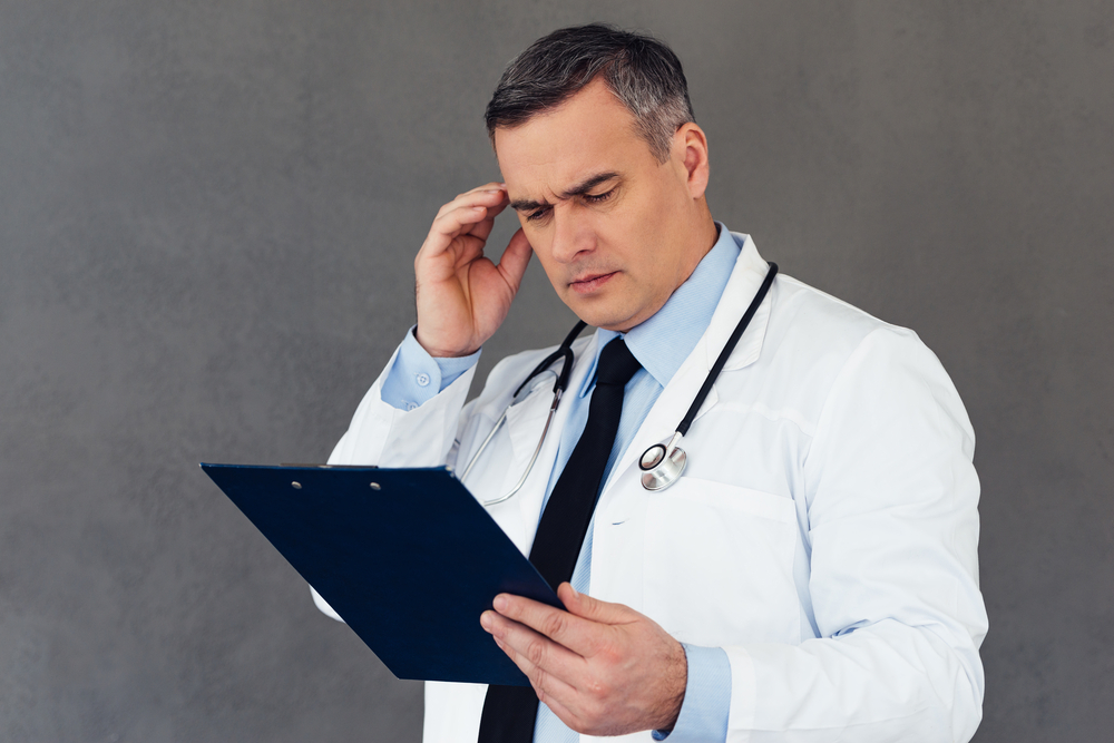 Mature male doctor looking at clipboard and looking confused
