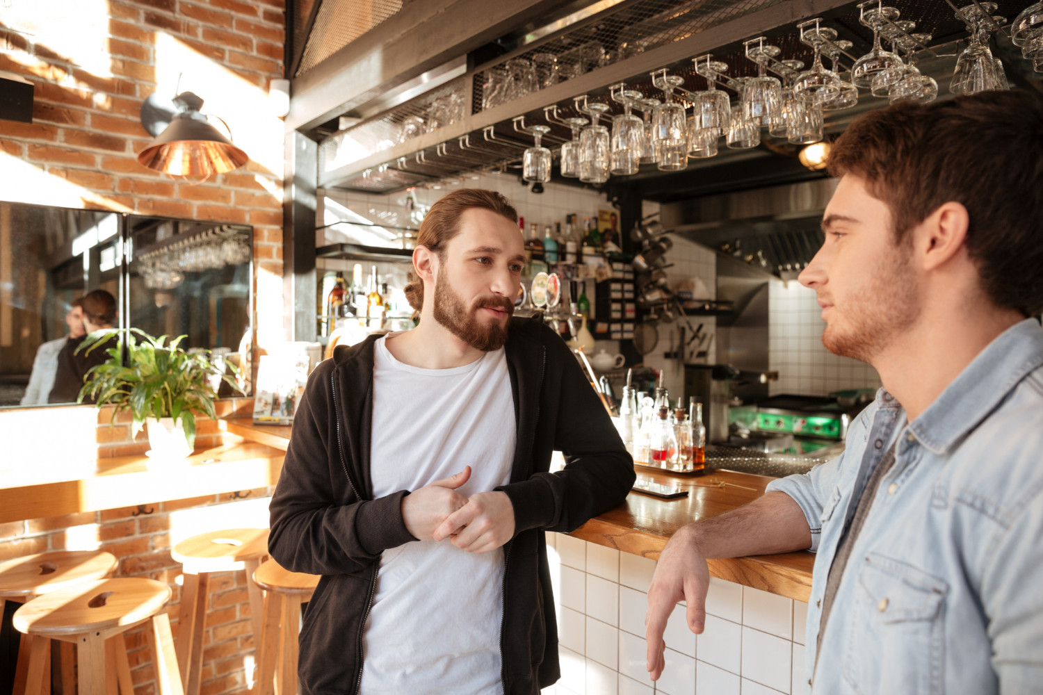 Two young man with beards are having a conversation at bar at restaurant.