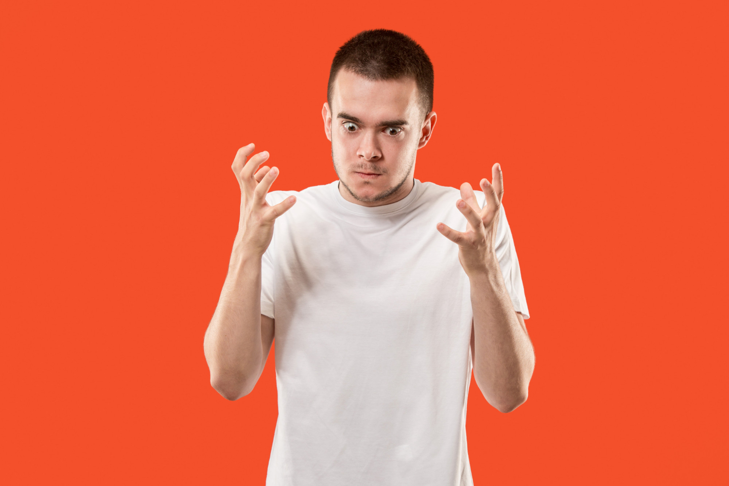Young man looking down with angry face on a red background.