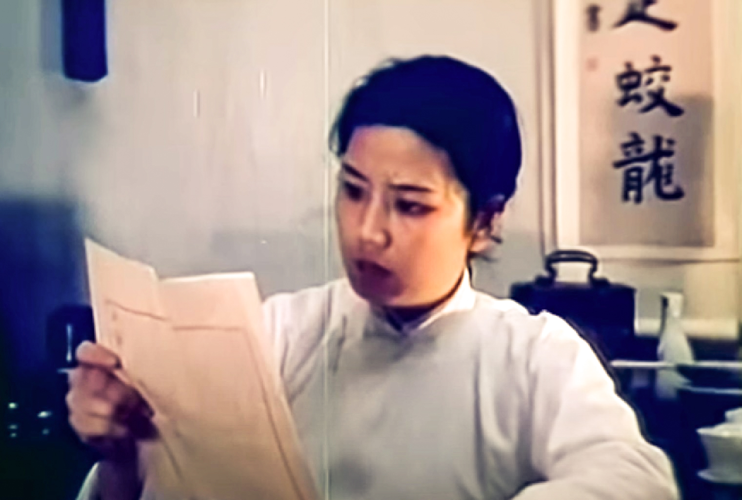 Screanshot: Qiu Jin (Xiuming Li) wearing white shirt is reading a paper - from Qiu Jin (1983)