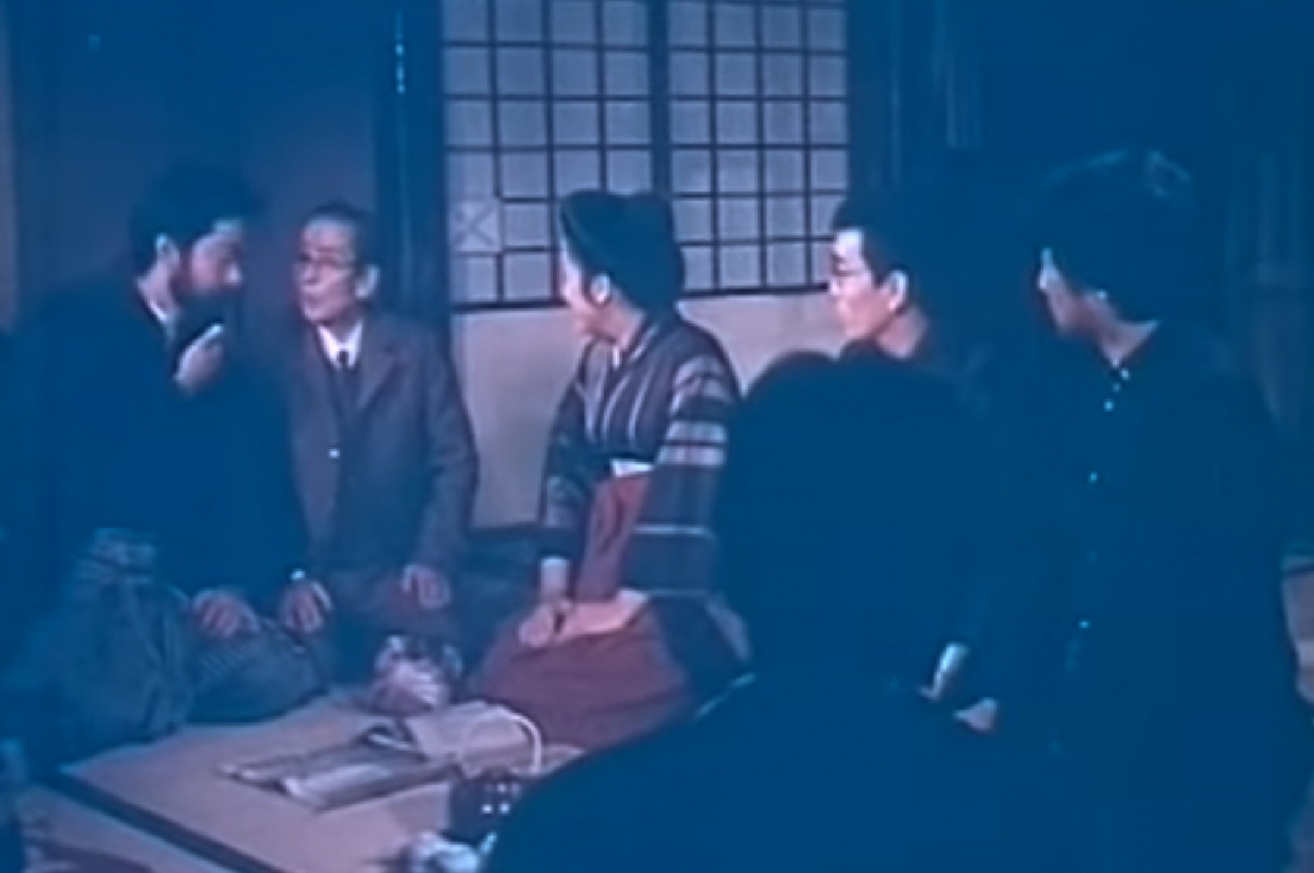 Screenshot: Qiu Jin (Xiuming Li) is seating in room with other people and talking - from Qiu Jin (1983)