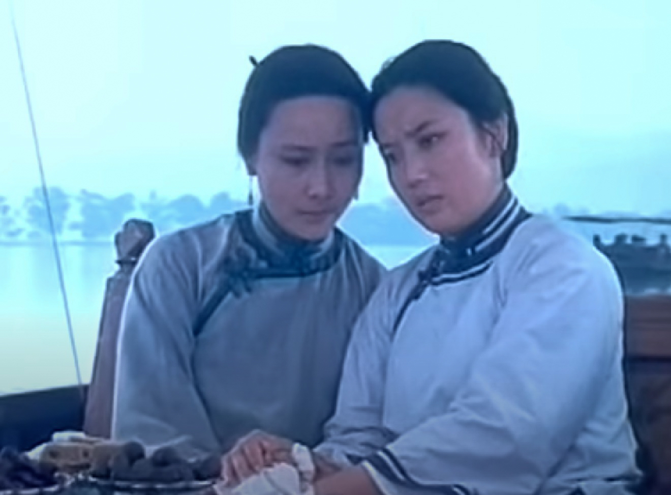Screenshot: Qiu Jin (Xiuming Li) is seating outside with other woman next to her ,looking sad - from Qiu Jin (1983)