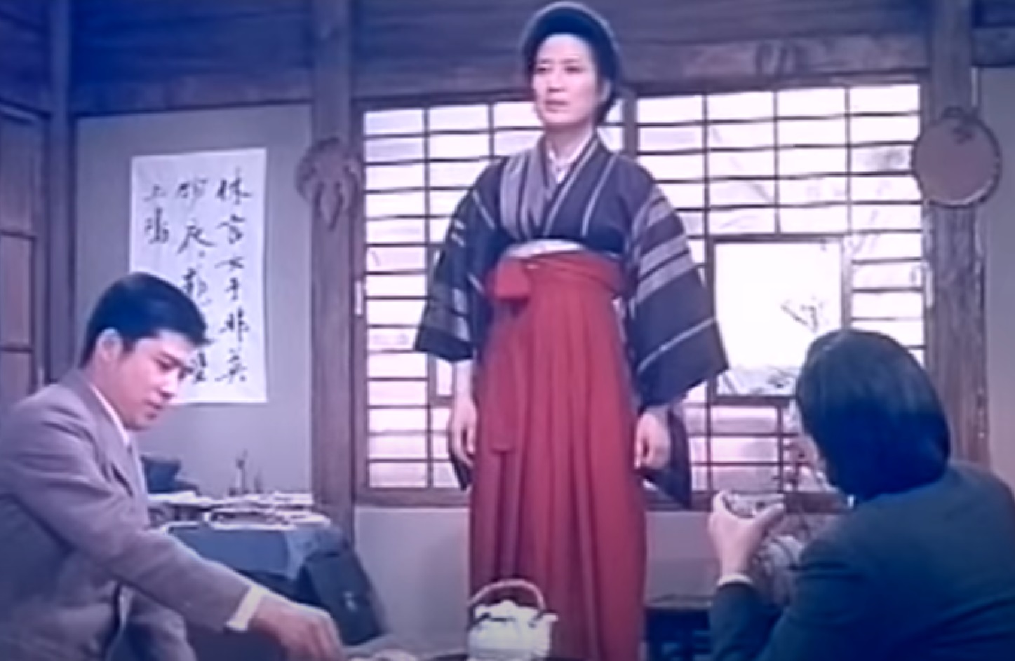 Screenshot: Qiu Jin (Xiuming Li) is standing and talking with other people in the room  - from Qiu Jin (1983)