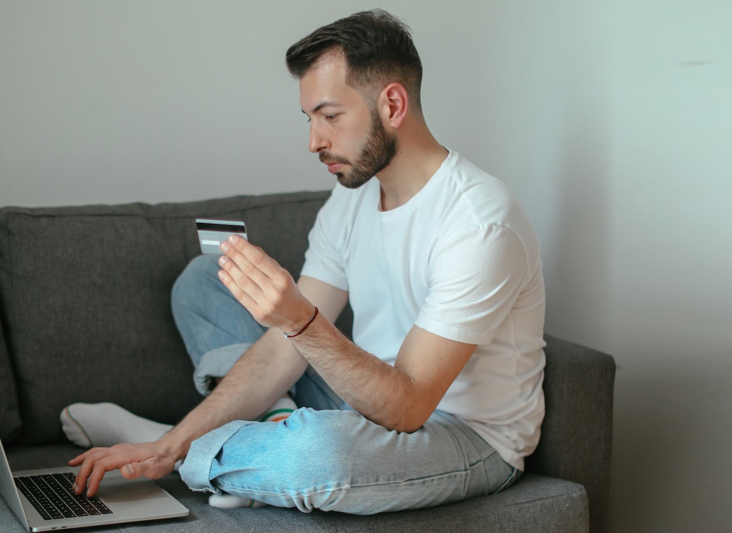 Man is seating on the sofa and making a payment on his laptop.