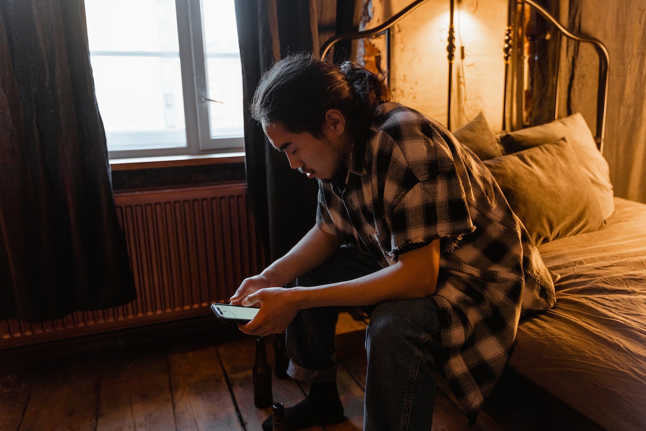 Man is seating on the bed and texting.