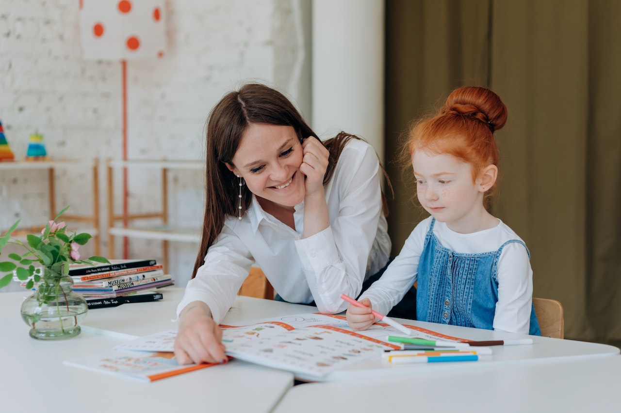 Female teacher is working with small girl at kindergarten.