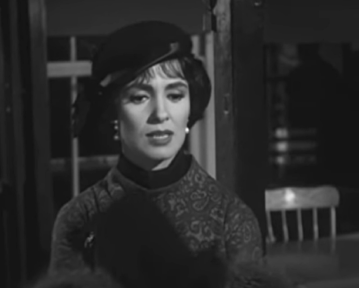 Screenshot: Susan Cabot wearing black dress and hat is looking down - from Machine-Gun Kelly (1958).
