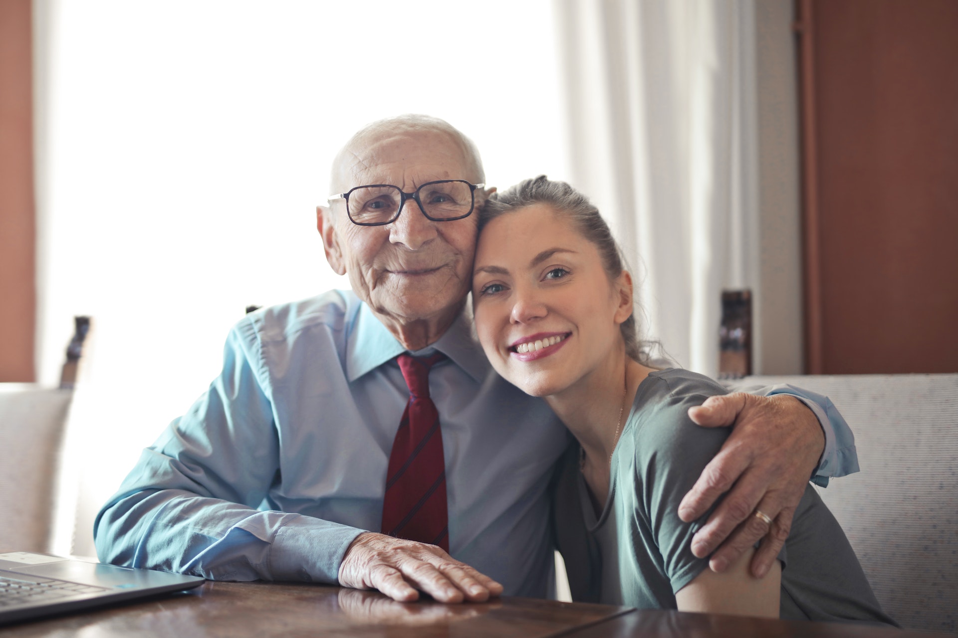 Positive senior man in formal wear and eyeglasses hugging young lady