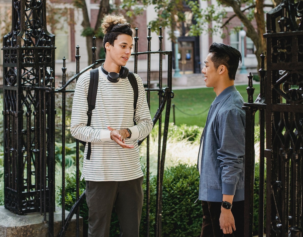 Two young man is standing outside and talking.